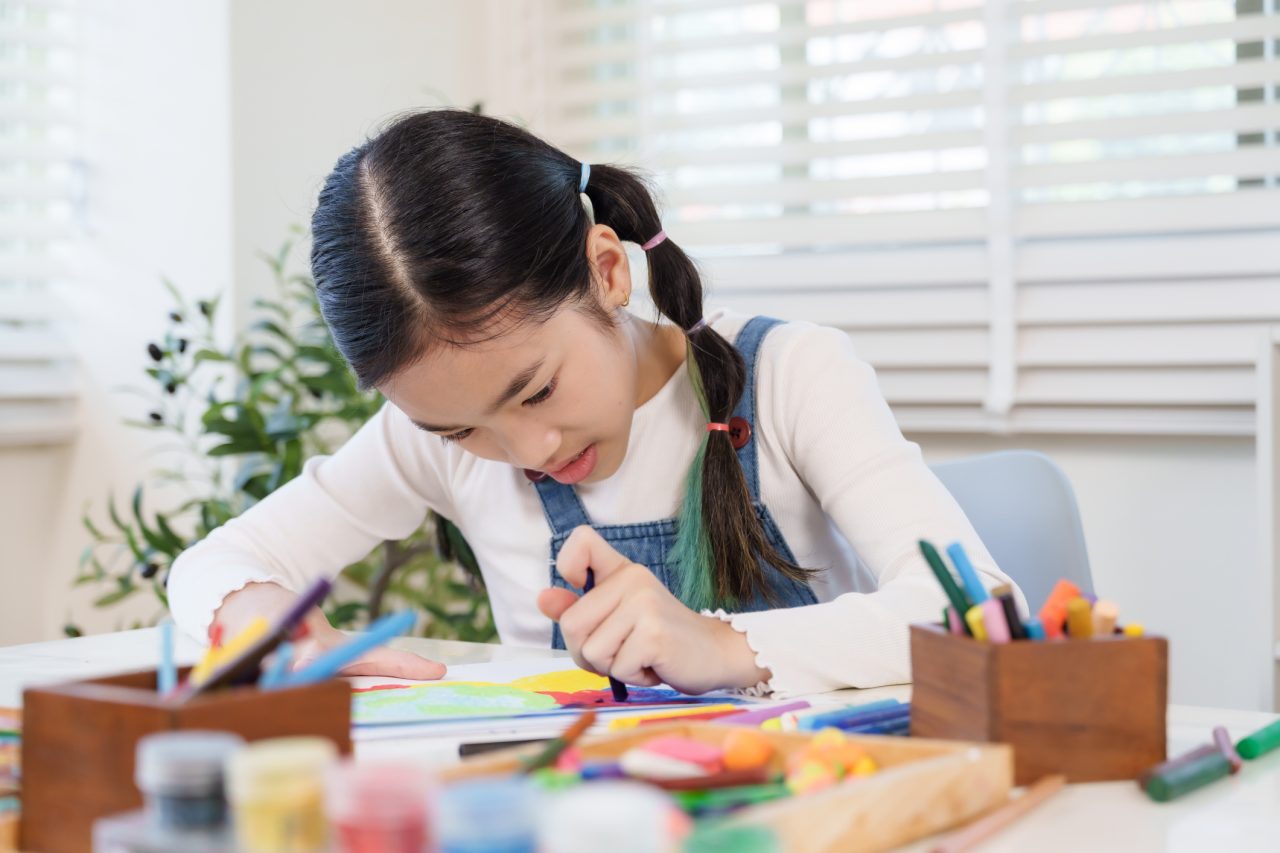 Child with ADHD working at a tidy, designated homework space with color-coded folders and a planner, checking off assignments to stay organized.